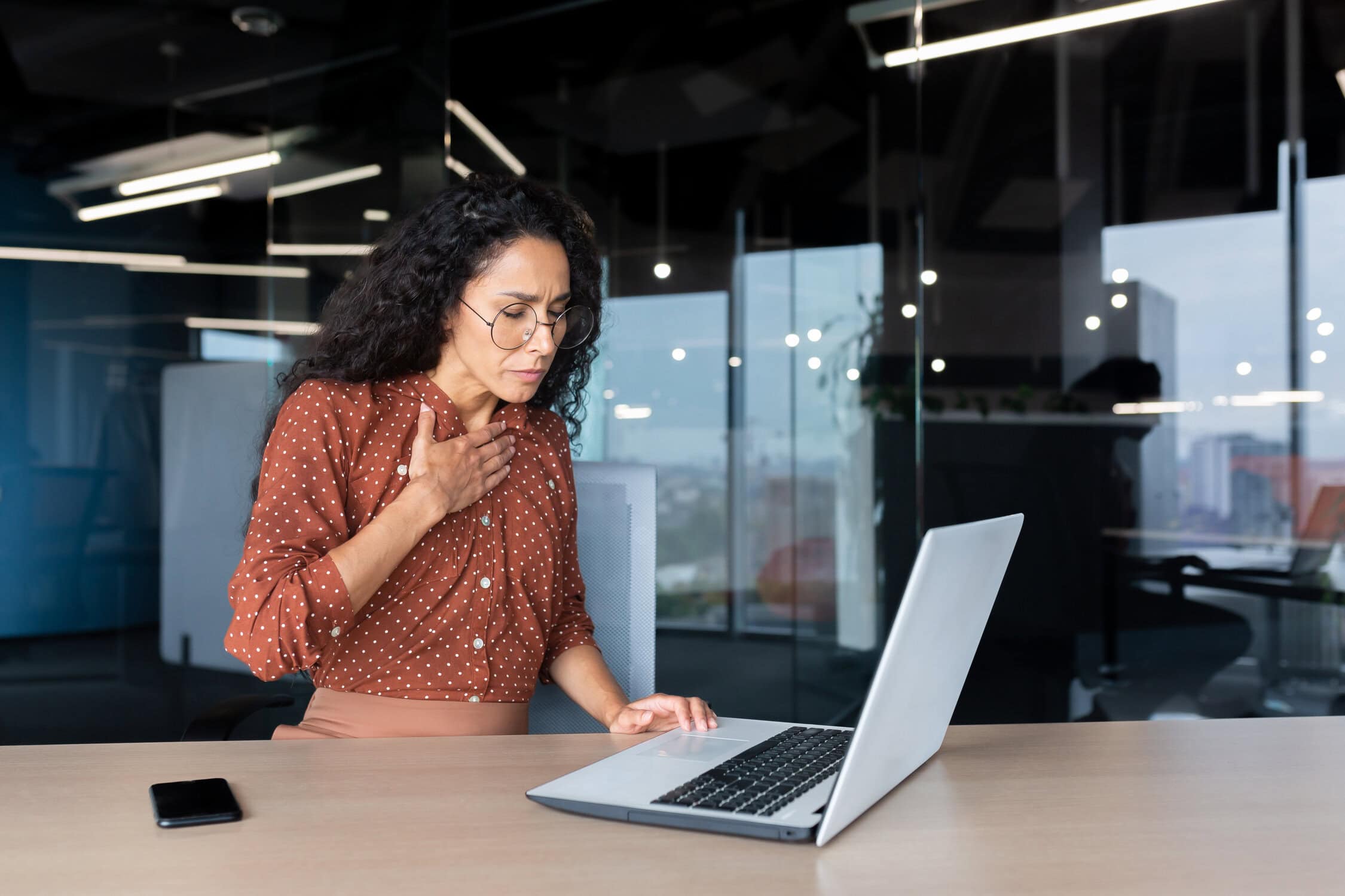 Ängstliche und verängstigte Geschäftsfrau, die in einem Büro arbeitet; hispanische Frau mit Panikattacke und Atemproblemen; weibliche Angestellte, die mit einem Laptop arbeitet.